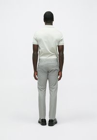 Gaiši pelēka polo krekls ar īsām piedurknēm, kombinēts ar pelēkām biksēm ar aizmugurējām kabatām un melnām kurpēm. Tīrs, vienkāršs dizains.