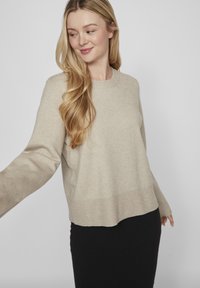 Šviesiai kreminis megztinis su apvaliu kaklu, ilgomis rankovėmis ir trumpu apačioje. Minkšta tekstūra ir trikampiai akcentai ant rankovių kraštų ir apatinės dalies.