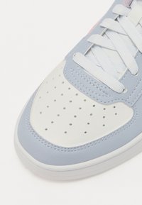 Lys blå og hvit sneakers med perforert tå, flate hvite lisser, overdel i lær, og en glatt teksturert såle. Har synlige sømdetaljer.