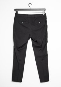 Svarta skräddarsydda byxor med en slät textur, med två bakfickor med knäppningar och design med rak ben. Hänger på en svart galge.