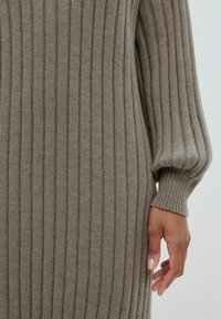 Graues Strickkleid mit vertikal gerippter Textur, langen Puffärmeln und taillierter Silhouette. Das Material wirkt weich und warm.