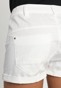 Vita bomullsshorts med uppvikta benslut, två bakfickor och synliga sömnadsdetaljer. Tyget har en mjuk textur.