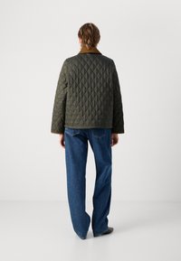 Gequiltede olijfgroene jas met een bruine kraag, met een rechte pasvorm en lange mouwen, gecombineerd met een blauwe wijde jeans.