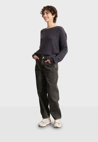 Suéter de punto waffle en color navy con mangas largas, combinado con jeans negros de cintura alta y zapatillas de color claro con un logo.