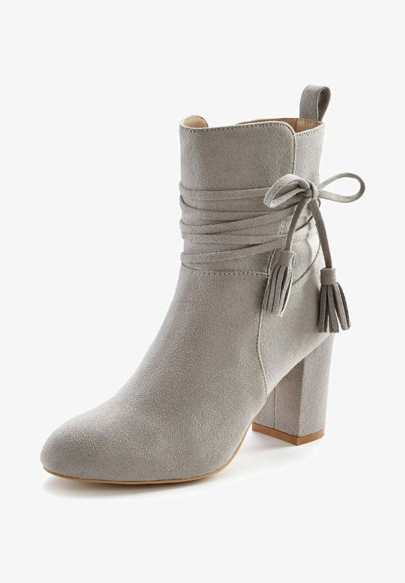 Bottine en daim gris clair avec talon bloc, lacets à pompons enroulés autour et languette à l'arrière.