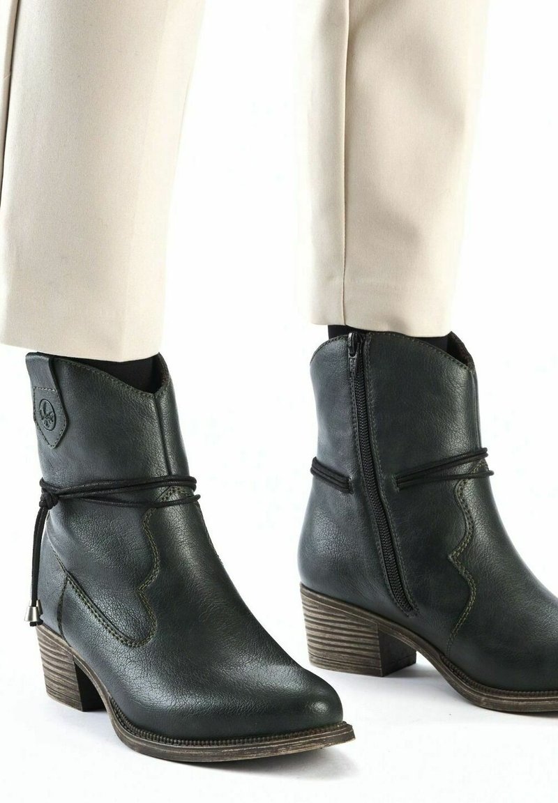 Botines de cuero negro con punta afilada, costuras decorativas, cremallera lateral y un tacón de madera más grueso. Diseñados con un detalle de cordones.