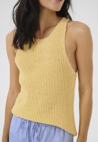 Geel gebreide tanktop met een structuurpatroon, voorzien van brede armsgaten en een losse pasvorm, gecombineerd met lichtblauwe joggingbroek met striksluiting.