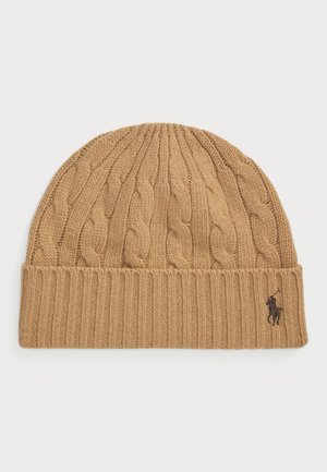 Knitted beanie in tan, featuring a cable pattern and a ribbed hem. Small embroidered logo on the front. Soft texture.