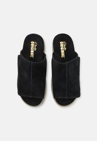 Sandali slip-on in suede nero con una ampia striscia, foderati con materiale morbido e dettagli cuciti. La suola è di colore chiaro e offre un'imbottitura per il comfort.