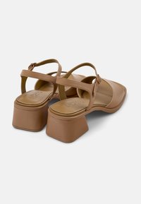 Ruske sintetiske sandale z blokastim petami, križnimi trakovi, kvadratnim noskom inoblazinjenim vložkom. Ima zaponko in gladko površino.