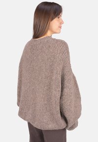 Übergroßer, gestrickter Pullover in weicher brauner Textur mit Rundhalsausschnitt und überschnittenen Schultern, der bis zu den Hüften reicht und mit gerippten Akzenten versehen ist.