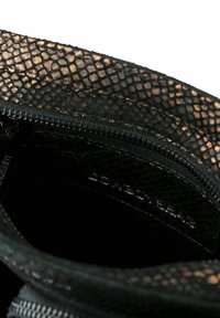Interno di una borsa nera con texture e motivo rettile, dotata di chiusura con zip. Presenta un rivestimento interno morbido di colore nero con un branding discreto.