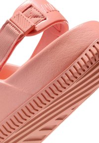 Sandale en caoutchouc rose avec une lanière texturée, dotée d'une boucle ajustable et d'une semelle crantée pour une meilleure adhérence. Surface lisse avec un branding subtil.