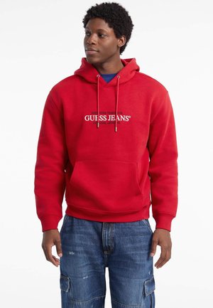 Haut à capuche en coton rouge avec une poche kangourou, des cordons ajustables et le logo "GUESS JEANS" en noir sur la poitrine.