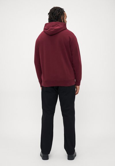 Camisola com capuz bordô, com cordão, costuras laterais e punhos canelados; combinada com calças pretas e sapatos pretos. Acabamento de tecido texturizado.