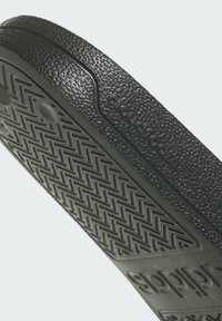 Svart cloudfoam-sula med texturerad yta, med ett zick-zack-mönster och präglad logotyp. Släta kanter och rundad form.