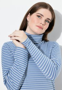 Blå randig polotröja med lång ärm och en figurnära design. Ränderna är vita på ett mjukt, texturerat tyg.