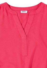 Blouse rose avec un col rond, une fente devant en forme de V et une étiquette blanche indiquant la marque "CECIL" à l'intérieur du col.