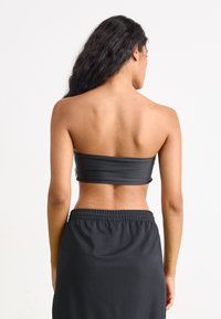 Top preto sem alças feito de material liso e elástico, combinado com uma saia preta de cintura elástica; textura suave, design simples.