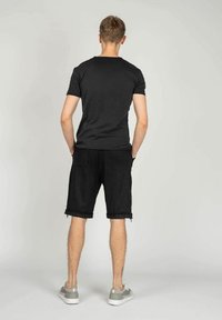 Sort bomuld t-shirt med korte ærmer parret med sorte shorts med frynset kant og sidelukninger. Grå sneakers fuldender looket.