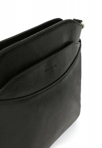 Borsa in pelle nera con una finitura testurizzata, dotata di una chiusura con cerniera superiore e una tasca curvata sul davanti. Dettagli di branding minimi.