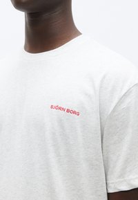 Ανοιχτό γκρι κοντομάνικο μπλουζάκι με στρογγυλή λαιμόκοψη, με κόκκινο λογότυπο "BJÖRN BORG" στο αριστερό μέρος του στήθους. Βαμβακερό ύφασμα με μαλακή υφή.