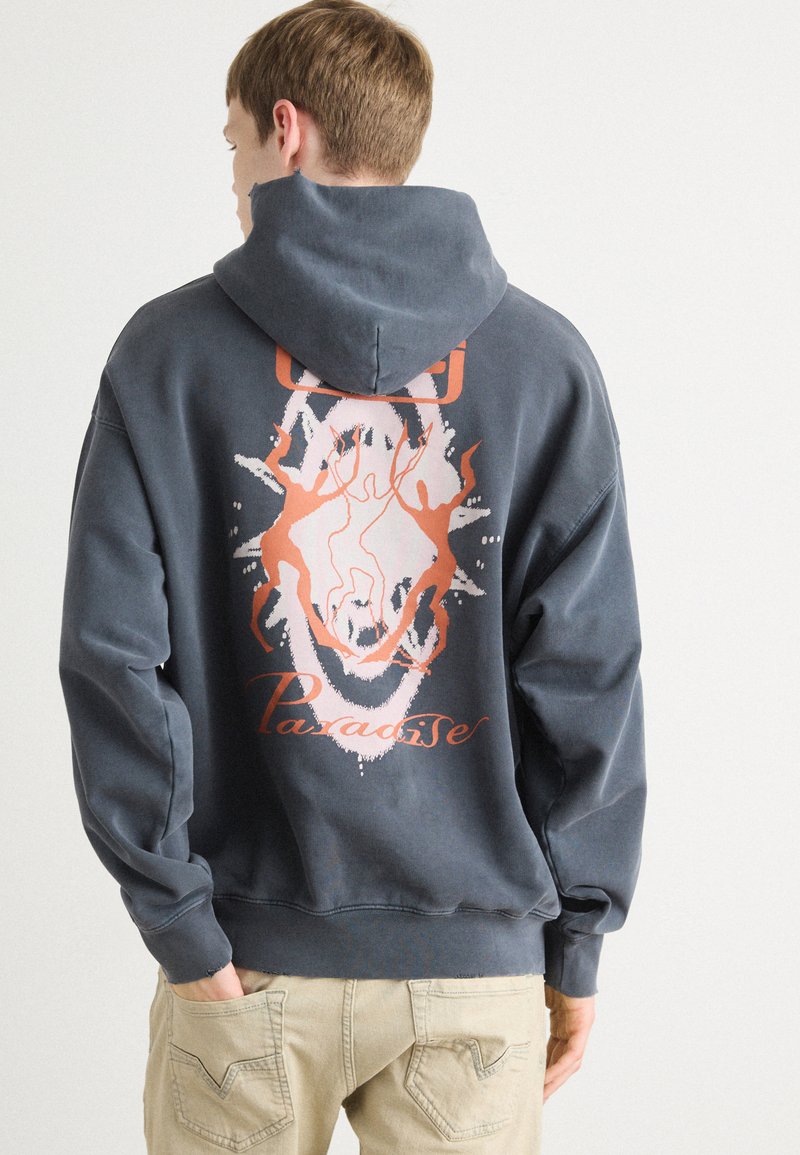 Sudadera gris con capucha, con un diseño gráfico en naranja y blanco en la parte posterior, que presenta formas abstractas y la palabra "Paradise".