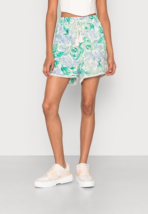 Pantaloni corti floreali con colori verde, blu e bianco. Presentano una vita con cordoncino e merletto lungo l'orlo. Abbinati a scarpe da ginnastica bianche chunky.