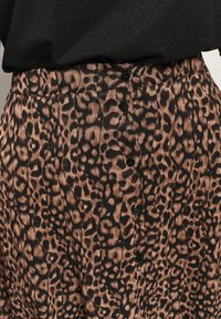 Jupe en imprimé léopard en tissu doux, avec une taille noire et cinq boutons noirs sur le devant. Design fluide et facile, avec un motif texturé.