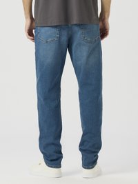 Hele sinised teksapüksid sirge sääre disainiga, millel on kaks tagataskut ja peened õmbluselemendid, kombineeritud valgete tennistega.