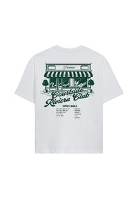 T-shirt blanc avec illustration verte d'une façade de café, texte "Courtside Riviera Club" et un menu café et bagel listant les options de boissons.