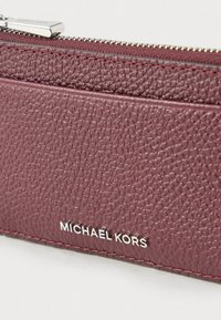 Burgundowa portmonetka wykonana z teksturowanej skóry, z zamknięciem na srebrny zamek błyskawiczny oraz metalicznym logo "Michael Kors" z przodu.