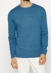 Blauer gestrickter Pullover mit Rundhalsausschnitt, langen Ärmeln und gerippten Bündchen. Aus einem weichen Stoff gefertigt, mit einem kleinen Logo auf der Brust.