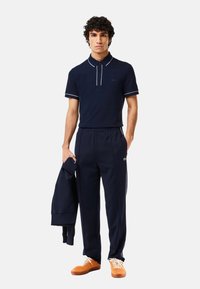 Marinblå polo skjorta med vita detaljer, i kombination med marinblå träningbyxor och oranga sneakers. Texturerad tyg med en logotyp på skjortan och byxorna.