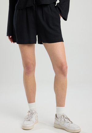 Black shorts with an elastic waistband, made of soft fabric. Paired with white sneakers and ribbed white ankle socks.