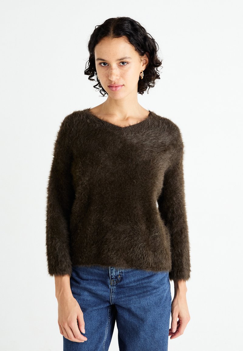 Hochgeschnittener brauner, flauschiger Pullover mit V-Ausschnitt, langen Ärmeln und weichem Material, kombiniert mit blauen Jeans. Einfaches und gemütliches Design.