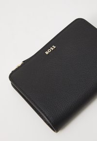 Black leather wallet with textured finish. Features a gold "BOSS" logo. Compact rectangular shape with a zip closure.
