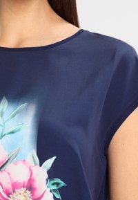 Marinblå topp med blommönster av rosa pioner och gröna blad. Kort ärm och en slät yta ger en figurnära passform.