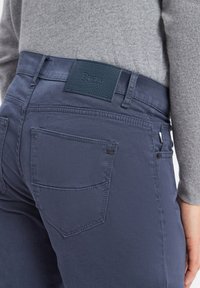 Pantalons bleu marine avec une taille texturée portant la marque "Brax", agrémentés de poches arrière et de détails de couture subtils.