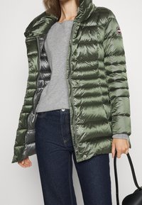 Green puffer coat with a high collar, made of glossy material, featuring quilted sections, a zipper closure, and snap buttons.