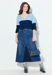 Suéter de punto color bloqueado en azul y marino con escote en V, combinado con una falda maxi de mezclilla que presenta un panel triangular. Botines plateados y un bolso.