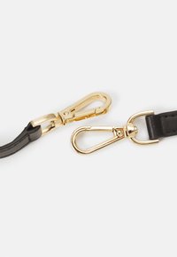 Černý kožený řemínek se zlatým kovovým kování. Kování obsahuje klips s pružinovým mechanismem a otočný háček.