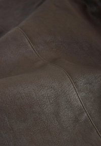 Material din piele maro cu un finisaj texturat, care prezintă cusături subtile și o suprafață netedă. Textura pare ușor uzată.