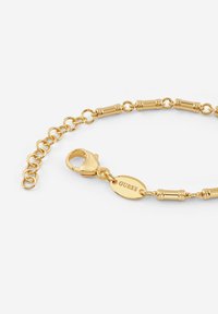 Gouden armband met langwerpige en buisvormige schakels, een scharnierslot en een merkoval charme. Glad metallic afwerking.