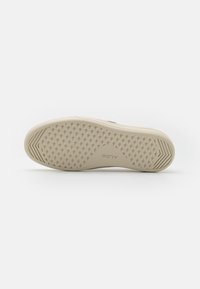 Sola della scarpa con una superficie in gomma beige strutturata che presenta un motivo triangolare e un logo in rilievo. Fianchi lisci con accenni di colore lungo i bordi.