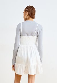 Vestido blanco de ropa con dobladillo con volantes y busto elástico. Superpuesto a una camiseta de manga larga de canalé gris claro. Textura de tela suave.