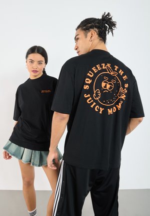 Sorte kortærmede t-shirts med orange grafisk tryk. En t-shirt har et legende orange karakter. En denim plisseret nederdel tilføjer kontrast.