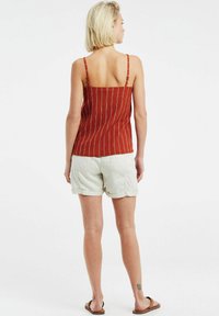 Camisola a righe rosse con spalline sottili, caratterizzata da un design aderente. Abbinata a pantaloni corti di colore chiaro e sandali piatti.