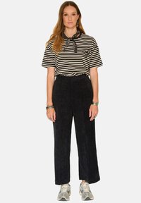 T-shirt rayé noir et blanc avec un foulard noir autour du cou, associé à un pantalon en velours côtelé large de couleur foncée et des baskets gris clair.