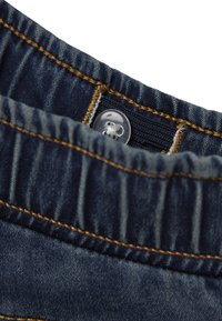 Mörkblå denimmidja med en synlig plastknapp och gula sömmar. Tyget har en mjuk textur med subtila veck.